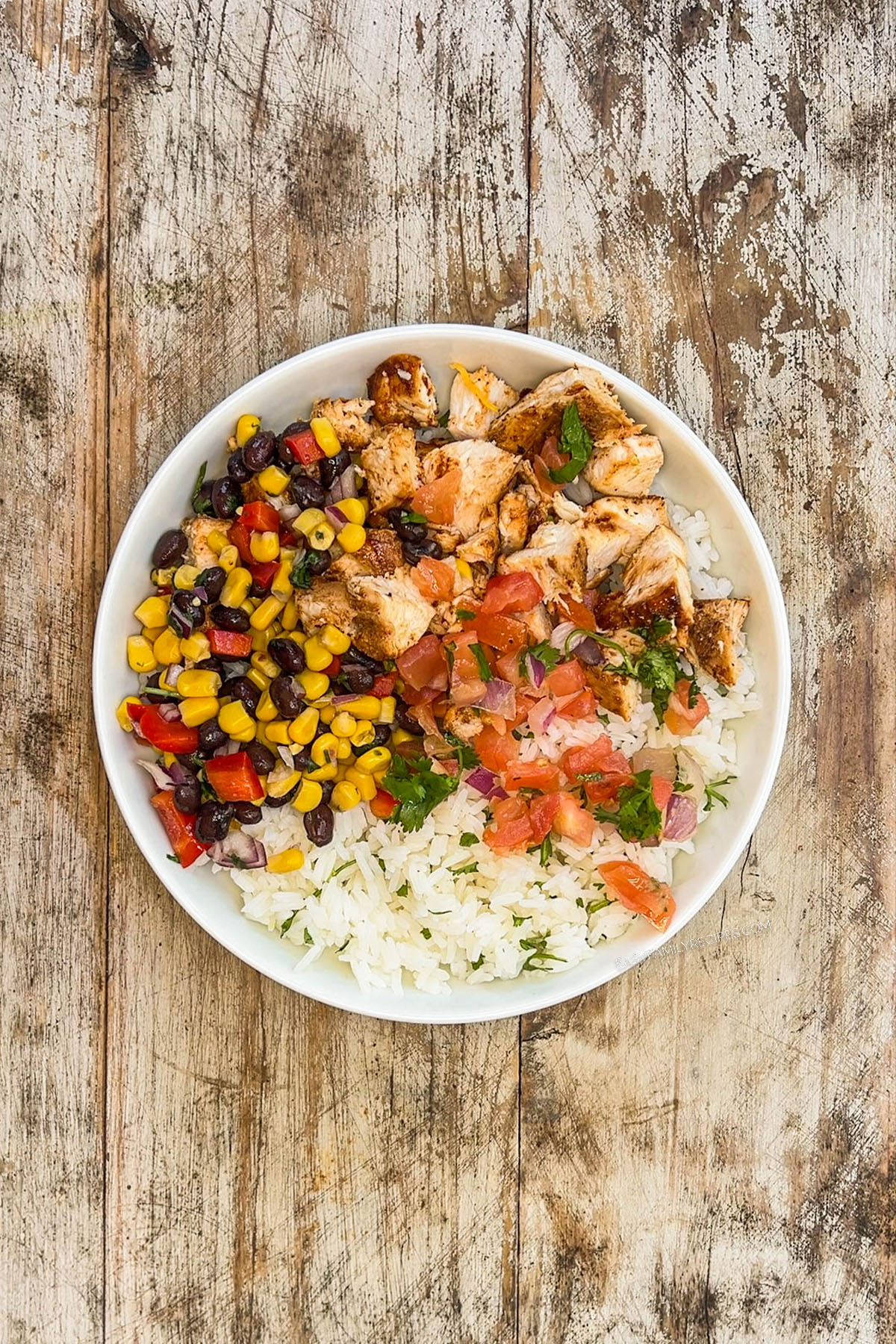 Step 3 of how to make BBQ chicken bowls: Add the salsa and pico de gallo. The ingredients are in a white bowl on a distressed wood background.