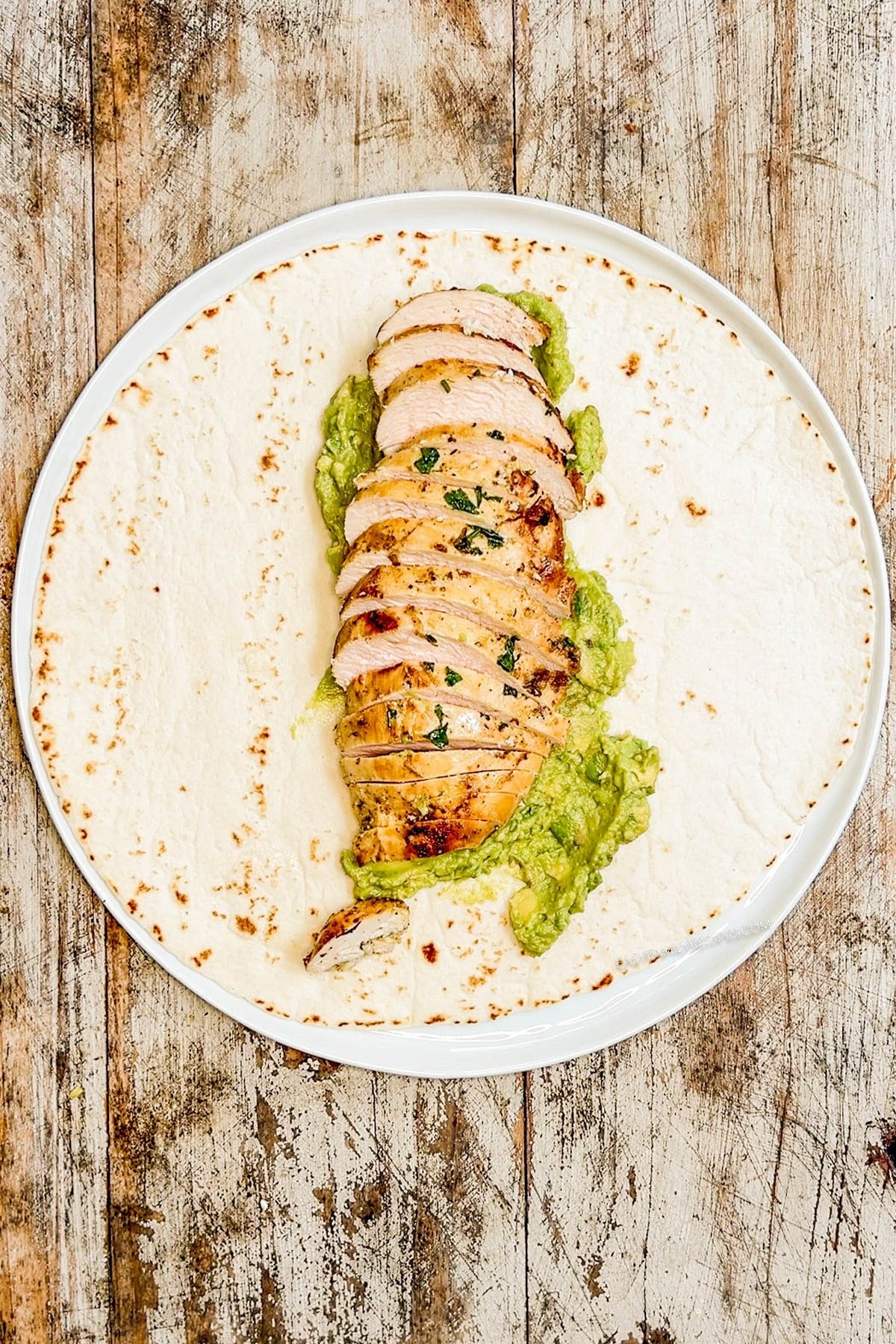 a tortilla on a plate with smashed avocado and cooked baja chicken.