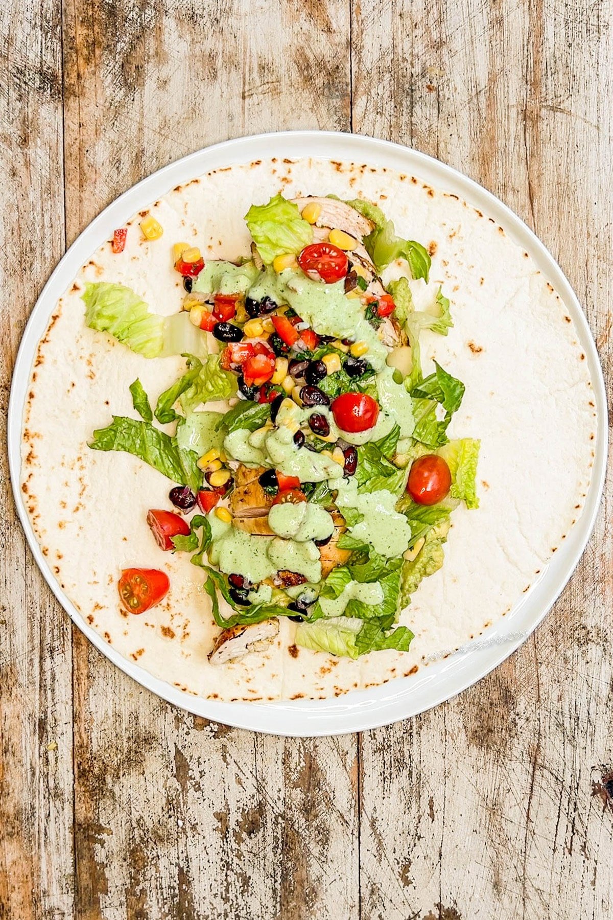 a tortilla on a plate topped with chicken and baja chicken wrap toppings.