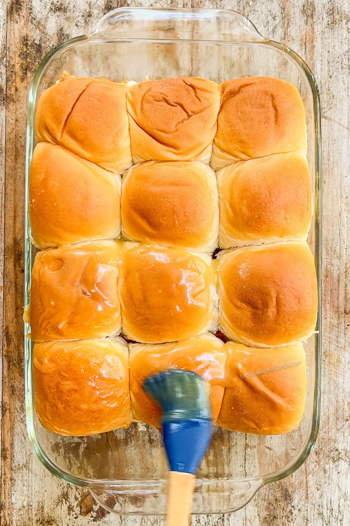 Brushing the tops of chicken tender sliders with honey Dijon butter sauce.