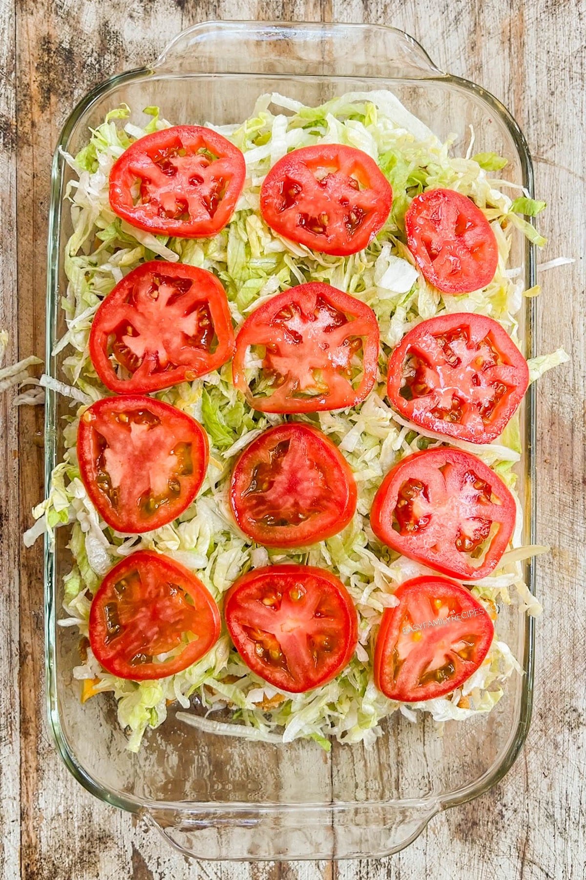 Adding lettuce and tomatoes to chicken tender sliders in a glass casserole dish.