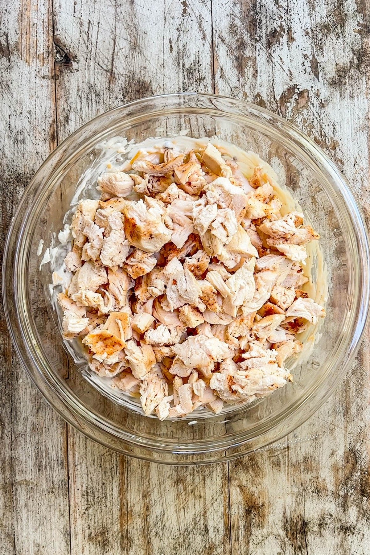 Chicken is added to a clear glass mixing bowl for Nixon Chicken.