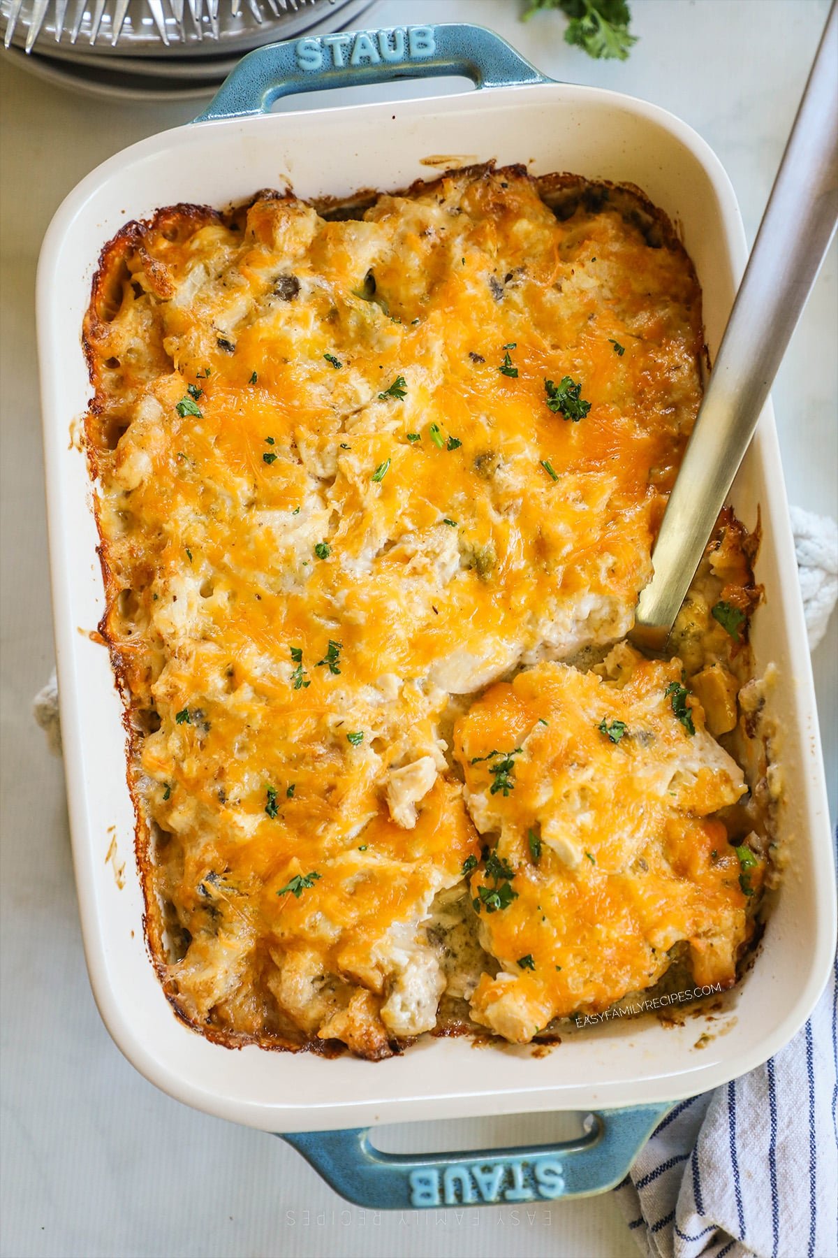 A large spoon scoops out a serving of Nixon Chicken from a white and teal baking dish. 