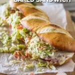 An Italian Grinder Sandwich sliced into sandwich-size pieces, wooden cutting board lined with parchment paper. The text reads, “Italian Grinder Baked Sandwich”