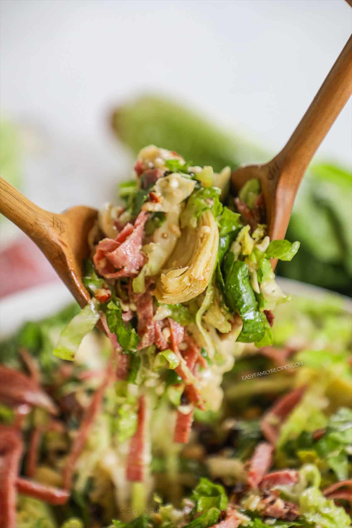 salad tongs lifting a big helping of la scala salad out of a bowl. 