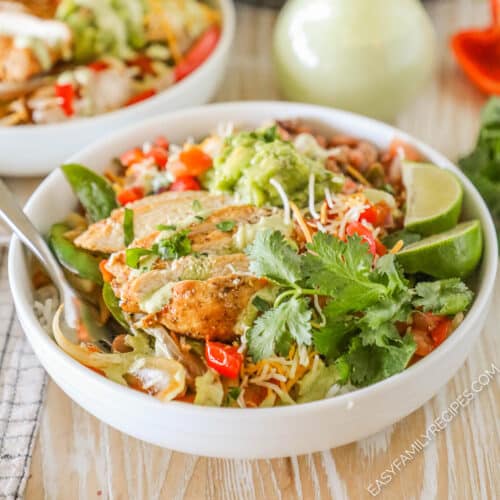 Chicken Fajita Bowls in a white bowl with a spoon and dressing alongside.