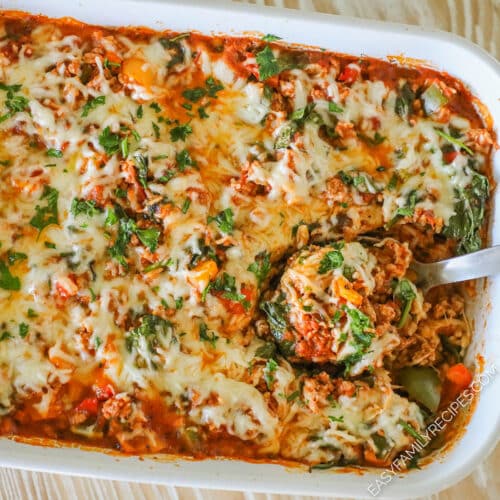 Turkey stuffed pepper casserole in a white casserole dish with a silver serving spoon scooping out a serving.