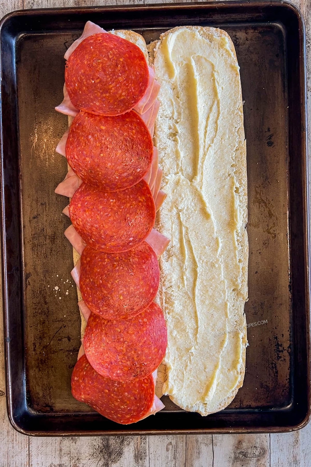 Step 1 for making Italian Grinder Sandwiches - slice French bread in half and spread with dressing and start laying the meat on the other side.