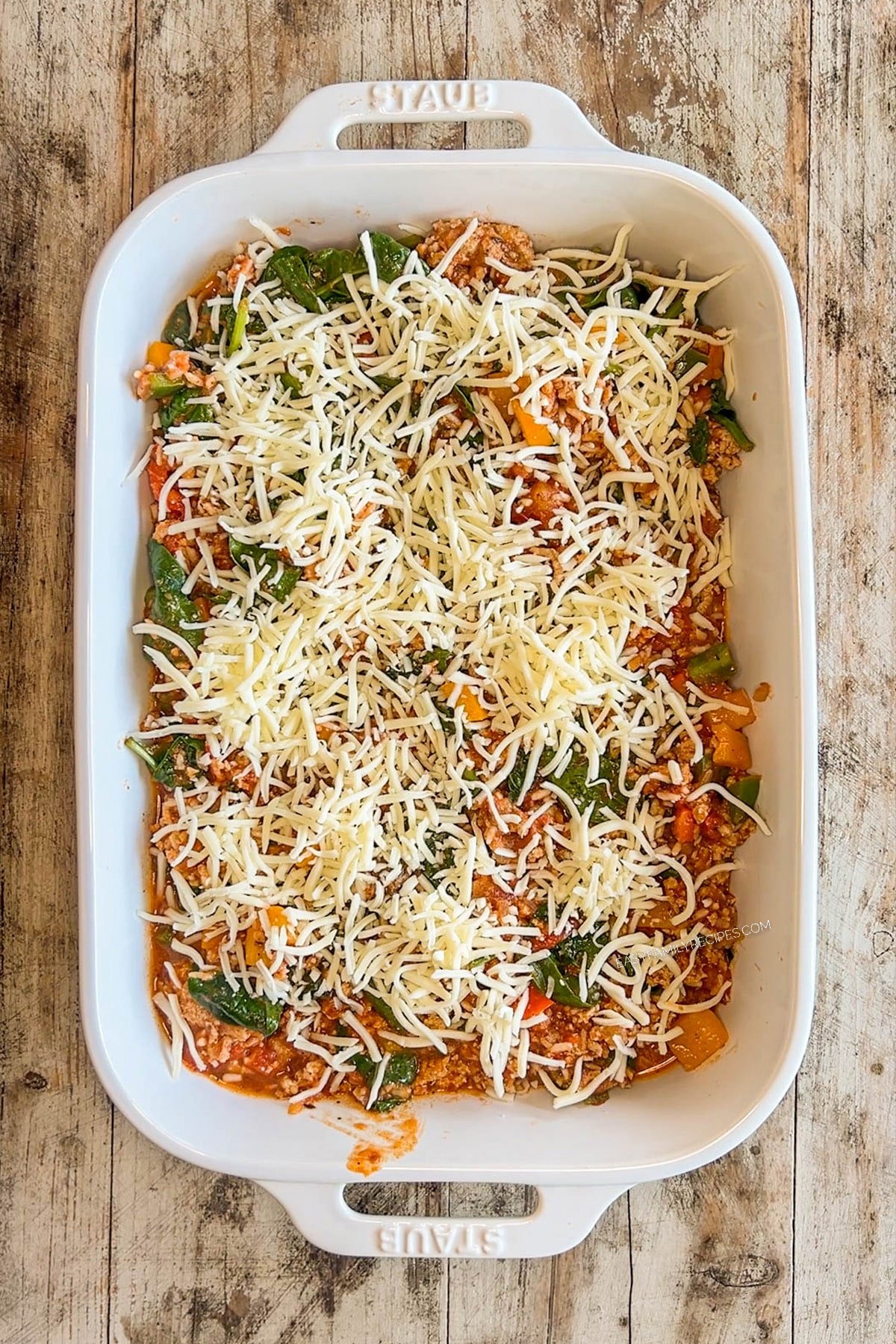 Turkey stuffed pepper casserole ingredients in a white casserole dish with cheese sprinkled on top.