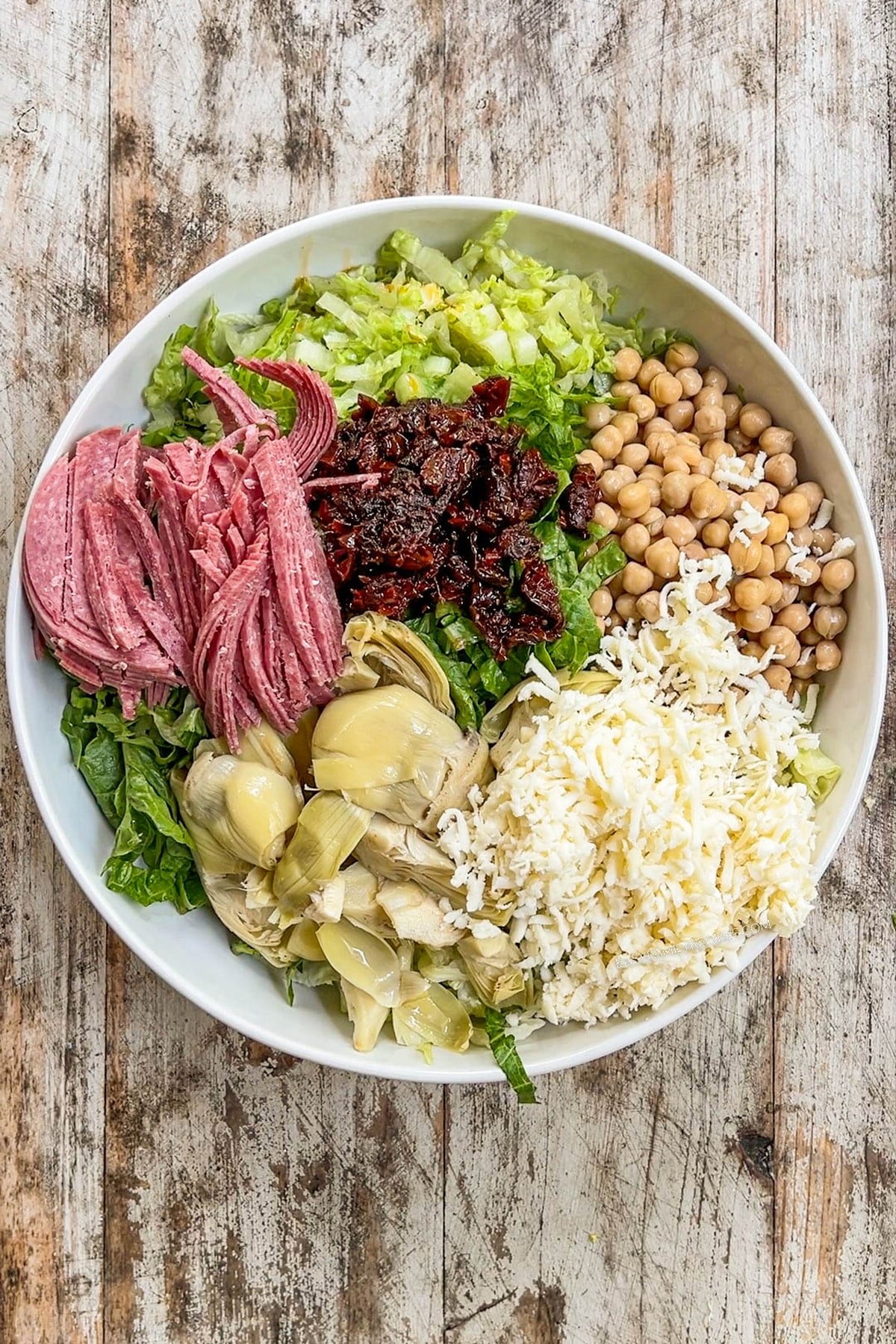 salami, chickpeas, sun dried tomatoes, artichokes, and cheese in a bowl.