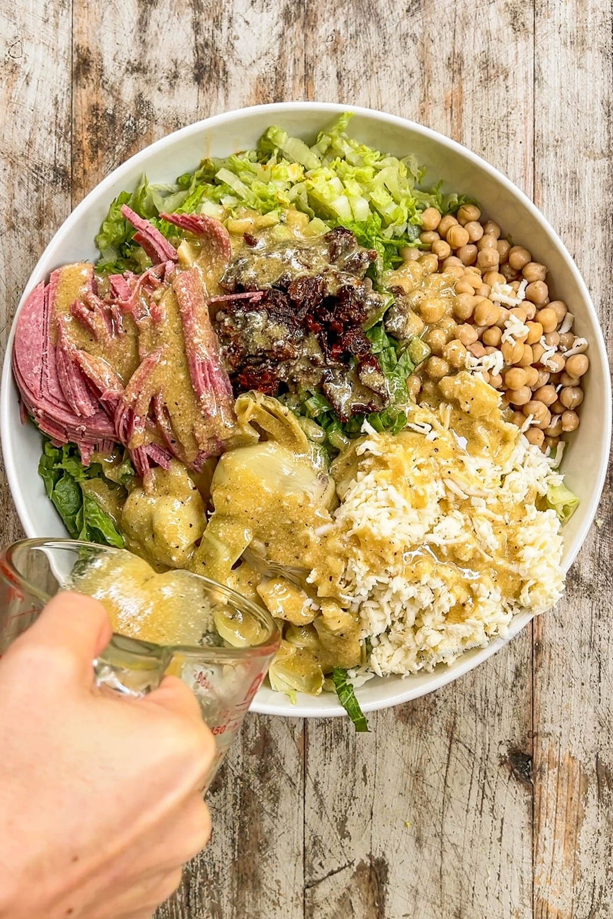 dressing being poured over a bowl of salad ingredients.