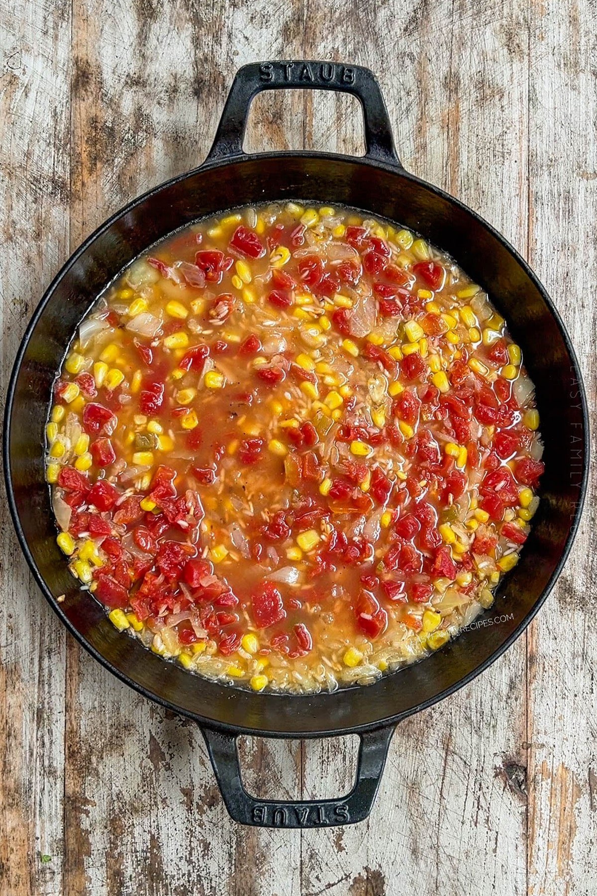 corn and tomatoes added to rice in a skillet.