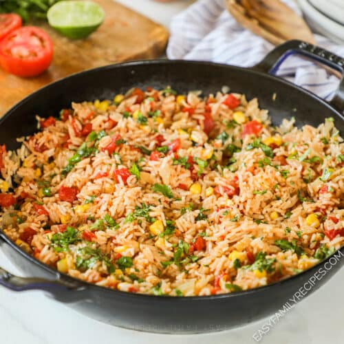 a skillet full of Southwest rice next to a cutting board with tomato and lime.