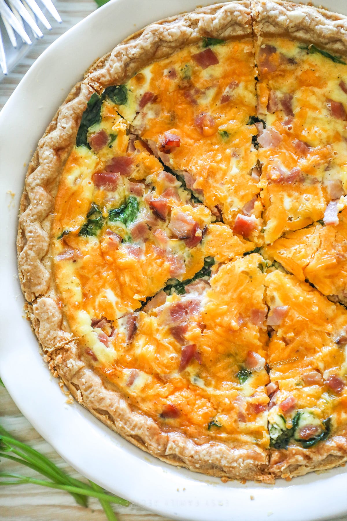 Top view of a ham and spinach quiche, sliced in to wedges, in a white pie dish