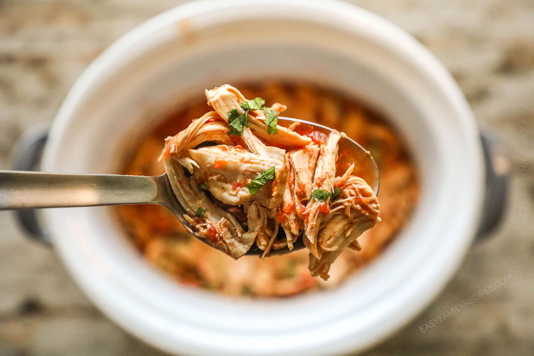 A silver spoon lifts out a serving of Crockpot Salsa Chicken.
