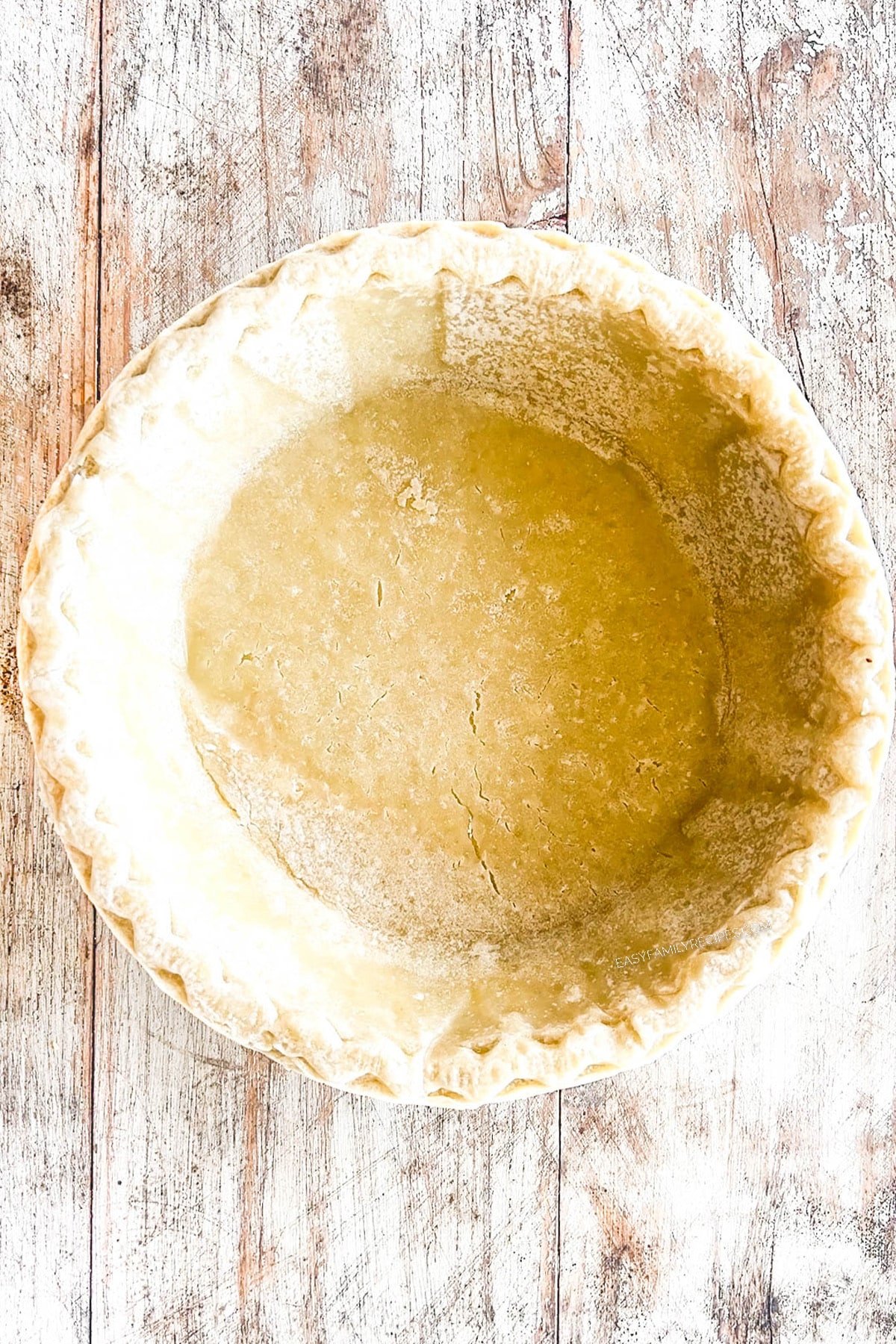 Pie crust is pressed into a white pie dish for quiche. Step 3 for how to make ham spinach quiche.