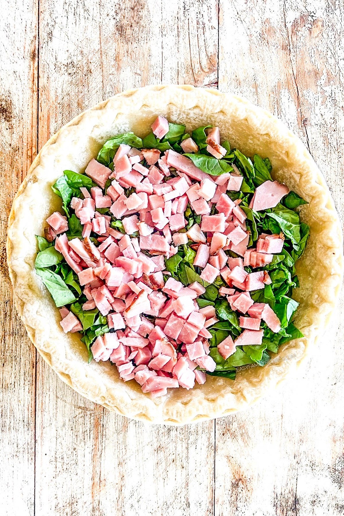 Step 4 for how to make ham spinach quiche. Spinach and ham are added to the pie crust.