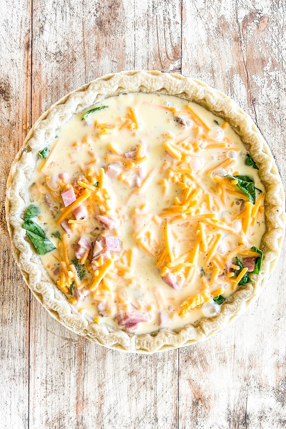 The eggs and cheese are poured over the ham and spinach for a ham and spinach quiche recipe. Step 5 for how to make ham spinach quiche.