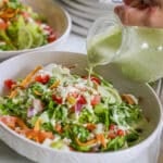 salsa verde ranch dressing being poured over an assembled tostada salad.