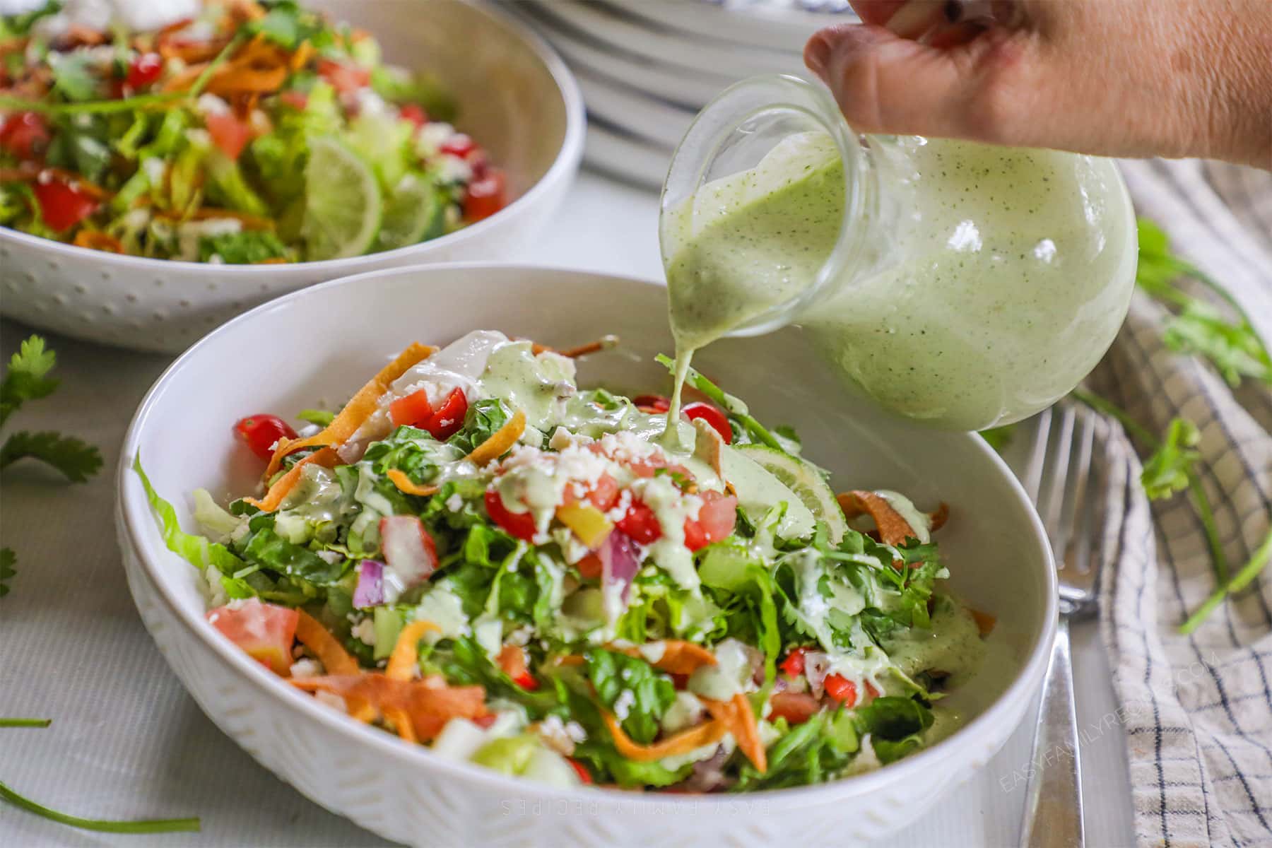 salsa verde ranch dressing being poured over an assembled tostada salad.