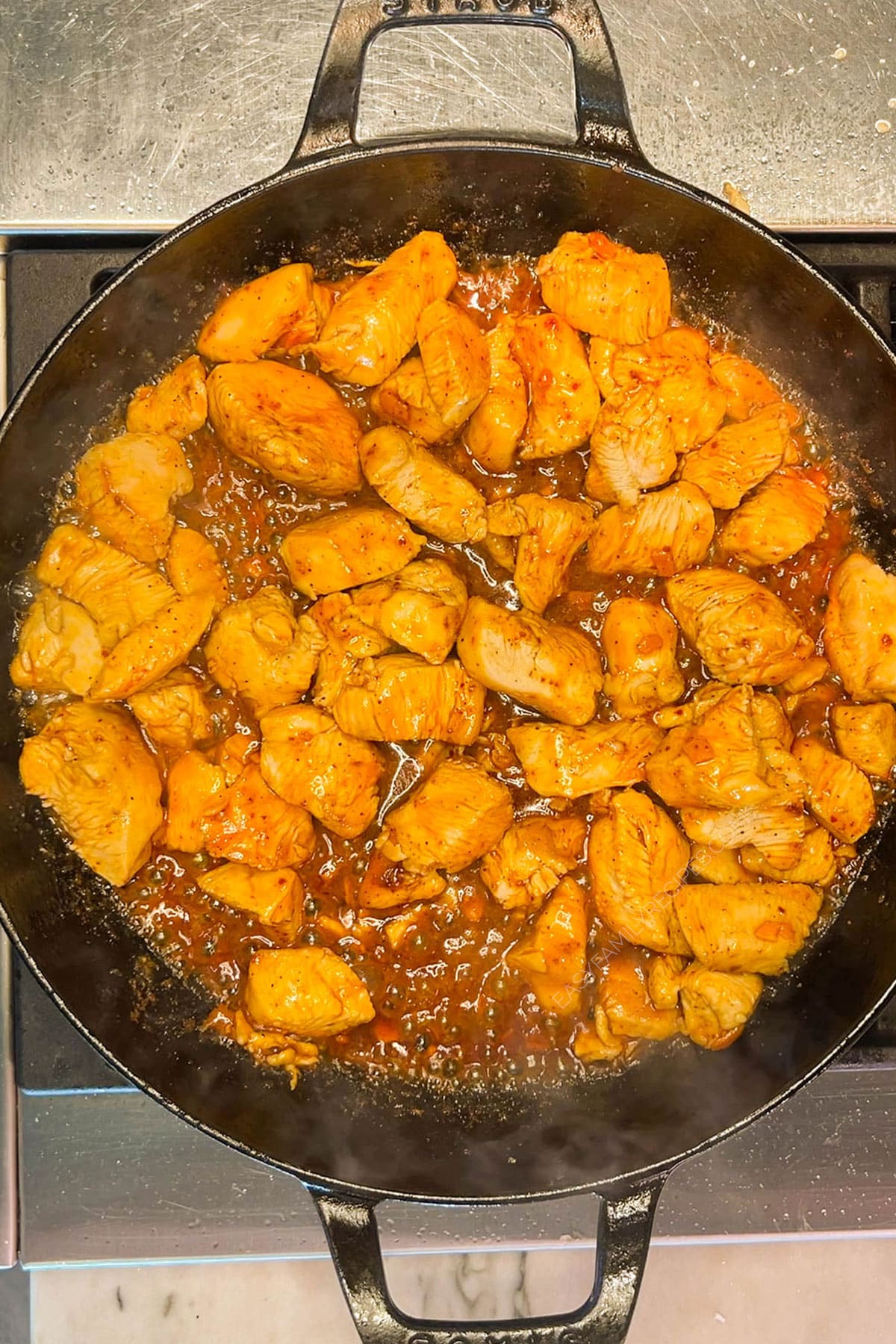 Chicken pieces in skillet after cooking with sauce.