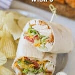 A chicken tender wrap cut in half with a skewer tucked into the top. It's on a white plate with potato chips on the side. The text reads, “Chicken Tender Wraps”