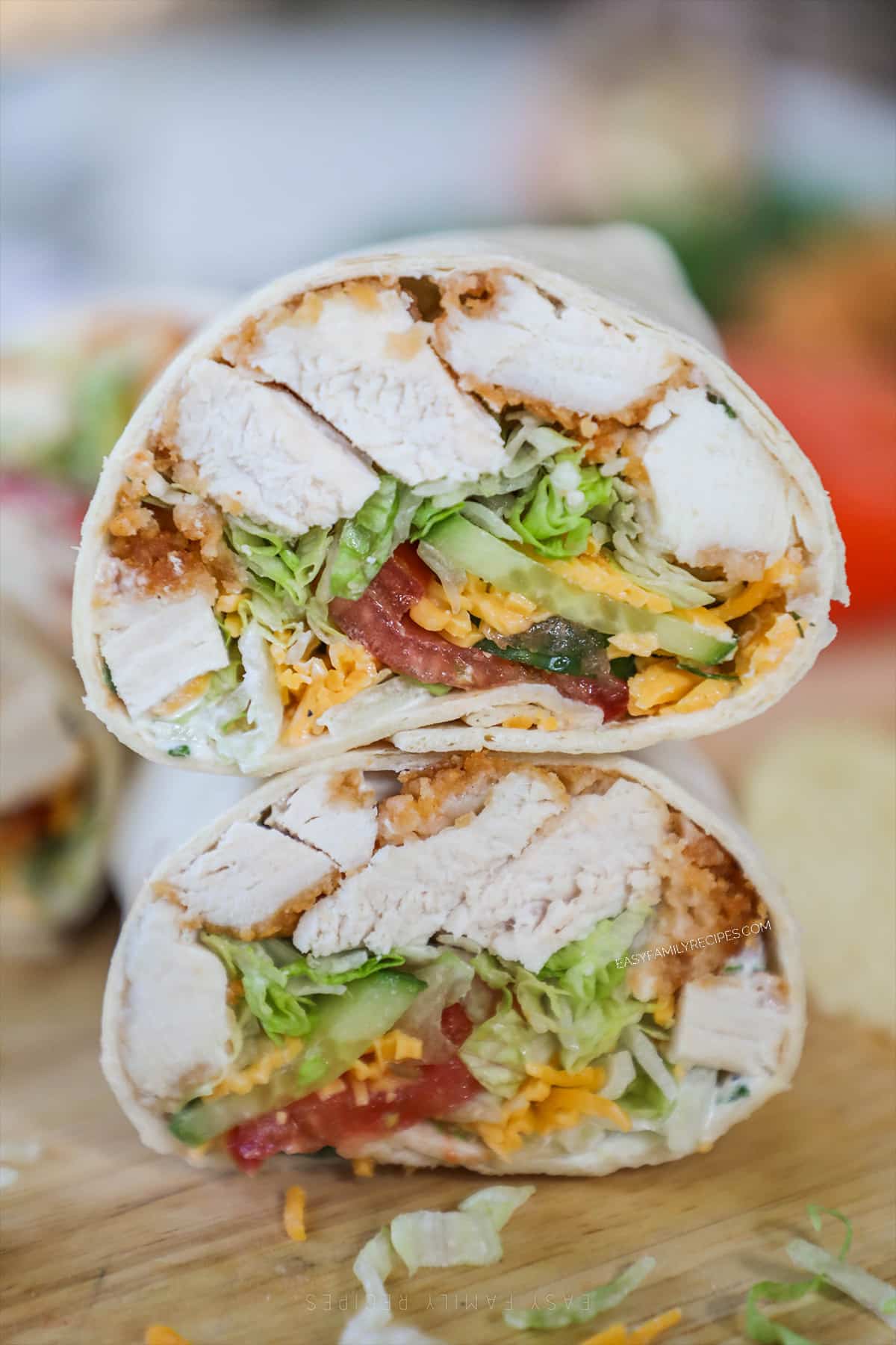 Chicken tender wrap cut in half and stacked on a wooden board.