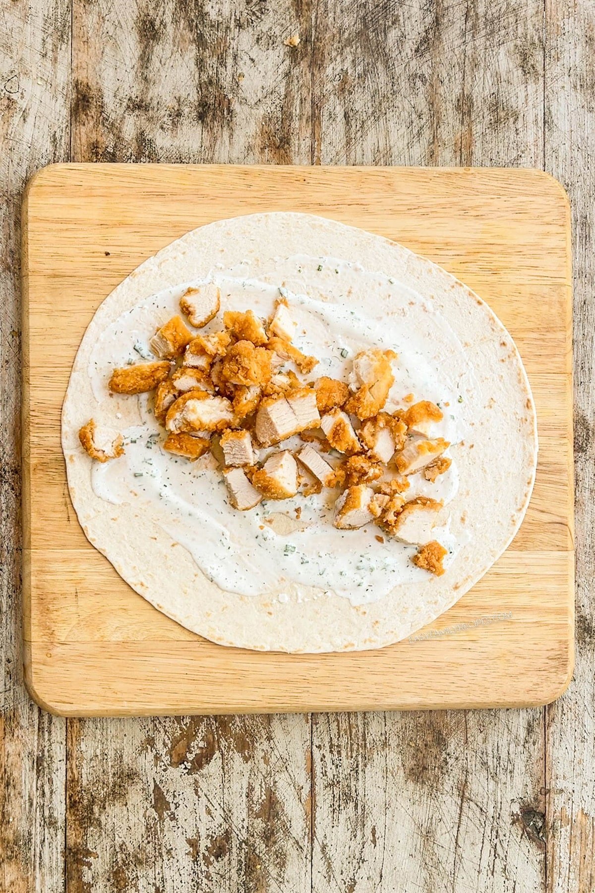 Step one for how to make chicken tender wraps: Spread the ranch and chicken in the middle of a tortilla wrap.