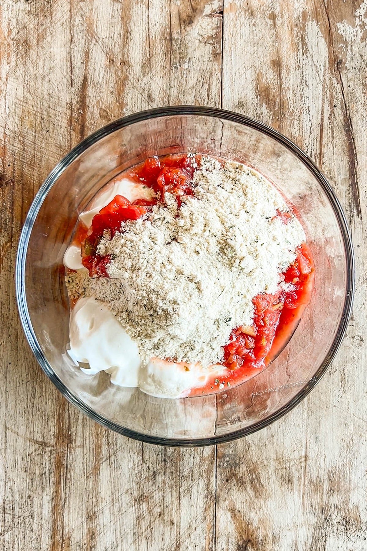 Mixing the dressing for layered taco salad in a clear glass mixing bowl.