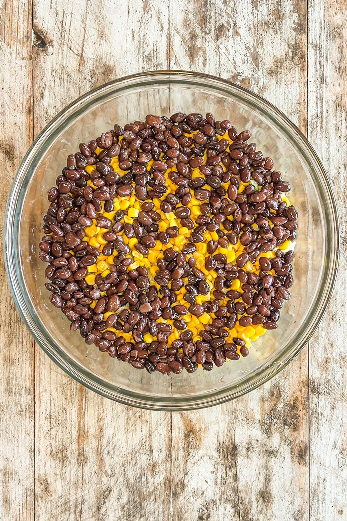 Beans and cheese are added to the glass bowl for layered taco salad