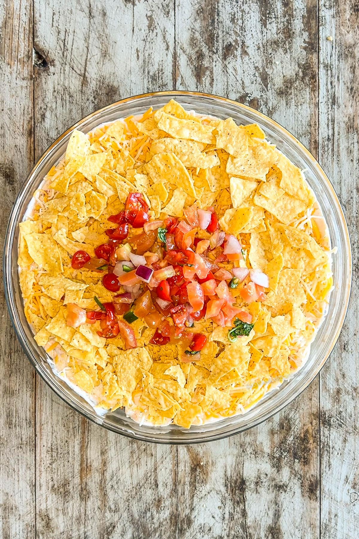 Crushed tortilla chips and a layer of tomatoes top layered taco salad