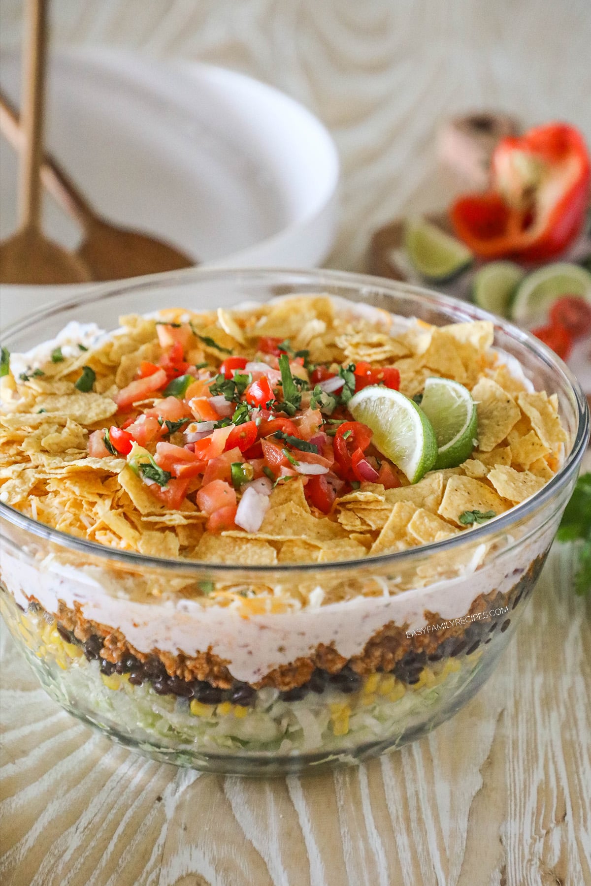 A glass bowl full of layered taco salad on a distressed wooden background.