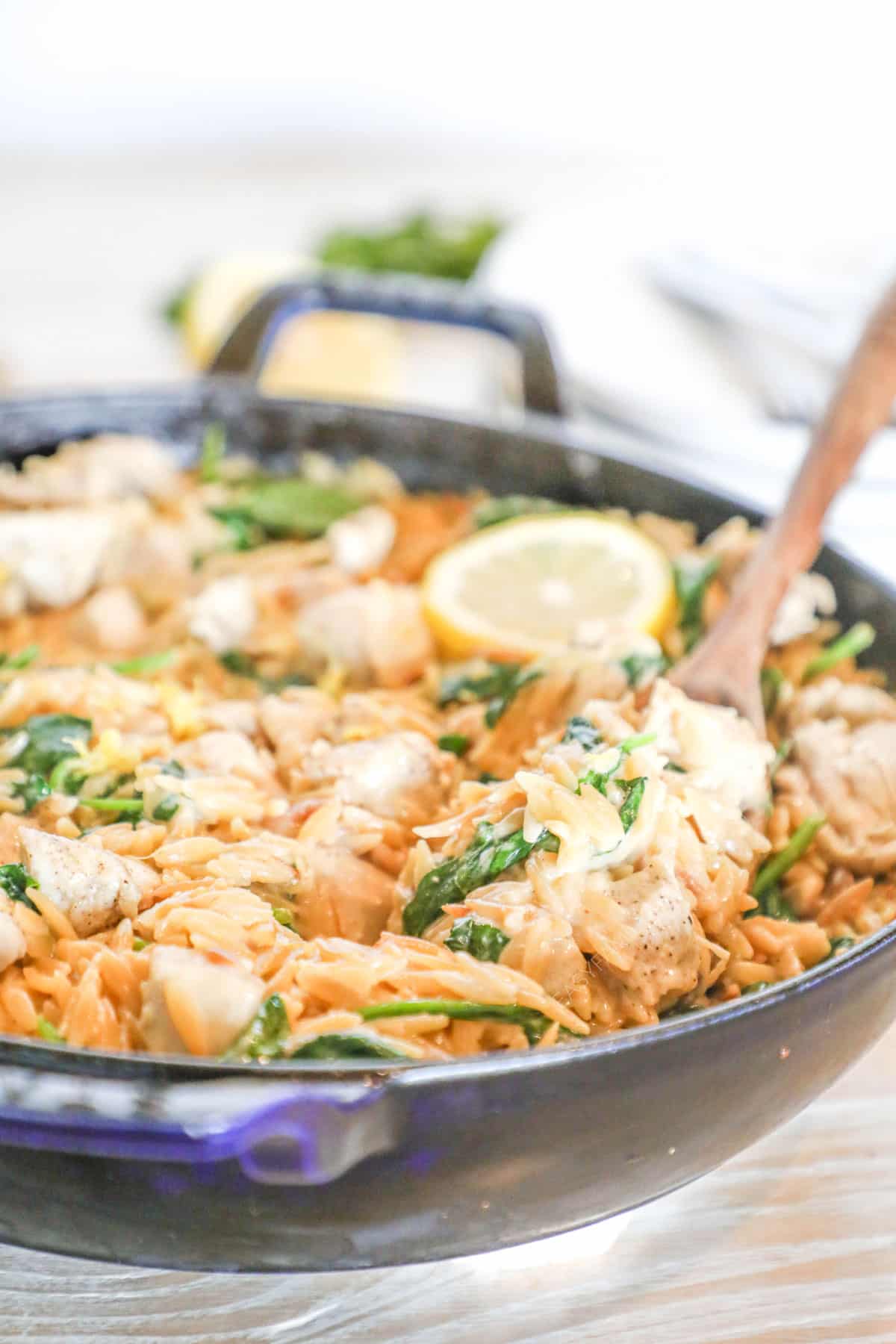 Creamy Lemon Chicken Orzo in a skillet with a wooden spoon and a lemon slice on top.