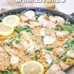 Creamy Lemon ORzo in a skillet with lemon slices and herbs on a whitewashed wood background. The text reads, "Creamy Lemon Chicken Orzo"