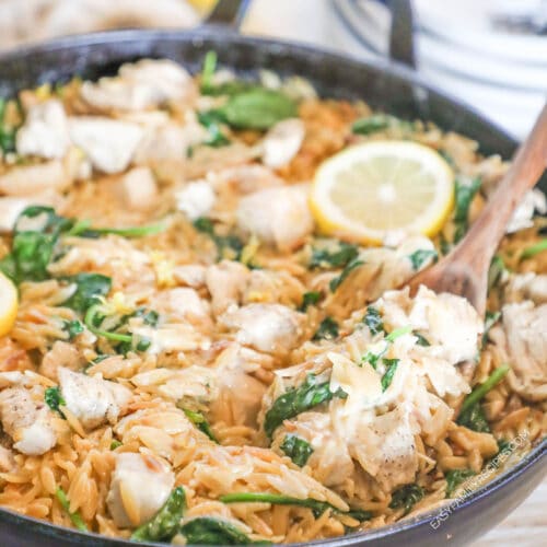 Creamy Lemon Chicken Orzo in a skillet with a wooden spoon and a lemon slice on top.