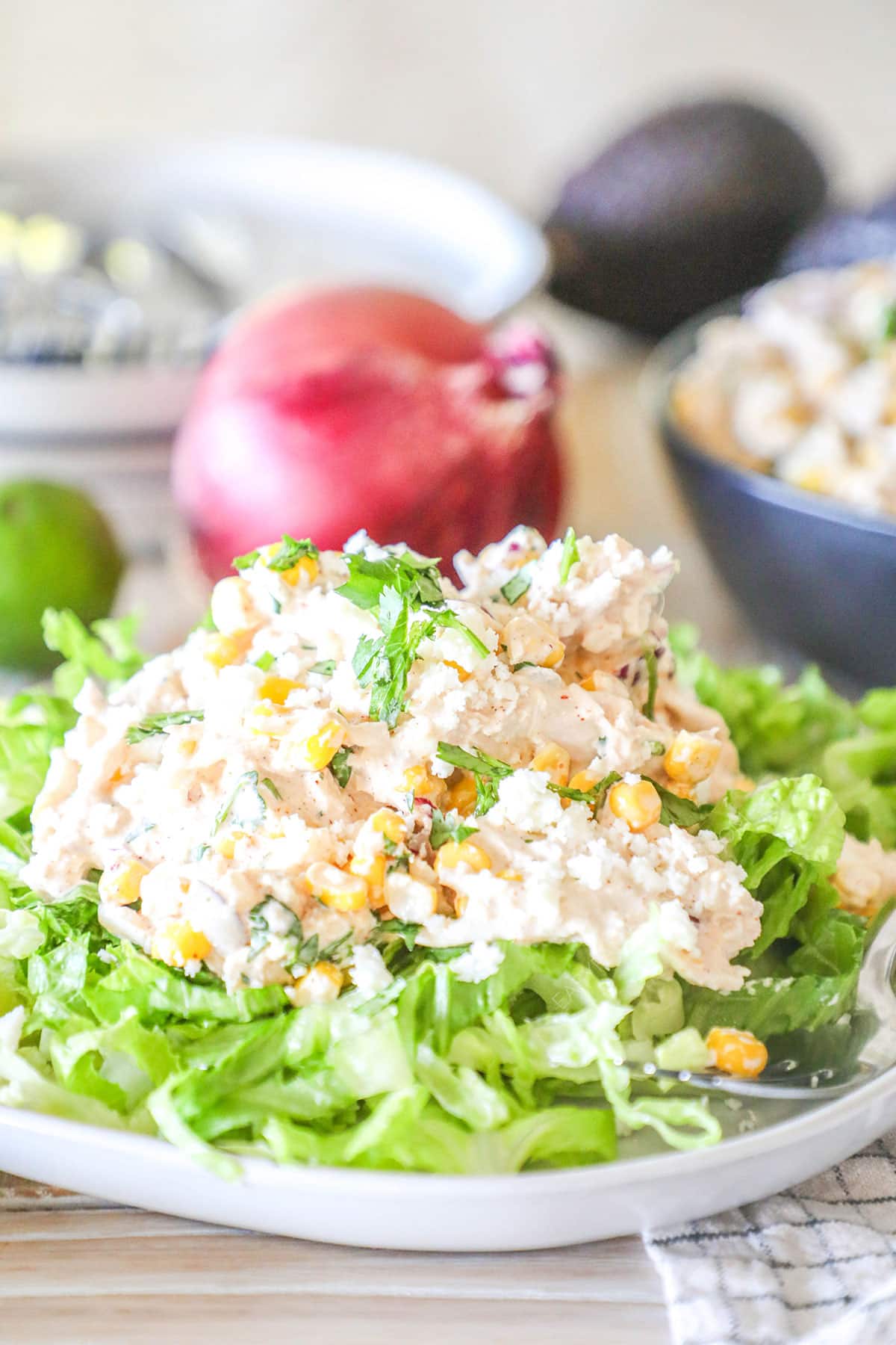 Street Corn Chicken Salad on a bed of fresh lettuce. A red onion is in the background.