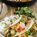 A white plate with Fajita Tacos and rice on a whitewashed wooden background. A skillet full of fajita chicken and veggies is in the background. The text reads, "A white plate with Fajita Tacos and rice on a whitewashed wooden background. A skillet full of fajita chicken and veggies is in the background. The text reads, "Fajita Tacos."