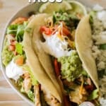 A white plate with fajita tacos on a whitewashed wooden background. The text reads, "chicken fajita tacos."