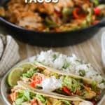 A white plate with Fajita Tacos and rice on a whitewashed wooden background. A skillet full of fajita chicken and veggies is in the background. The text reads, "A white plate with Fajita Tacos and rice on a whitewashed wooden background. A skillet full of fajita chicken and veggies is in the background. The text reads, "Fajita Tacos."