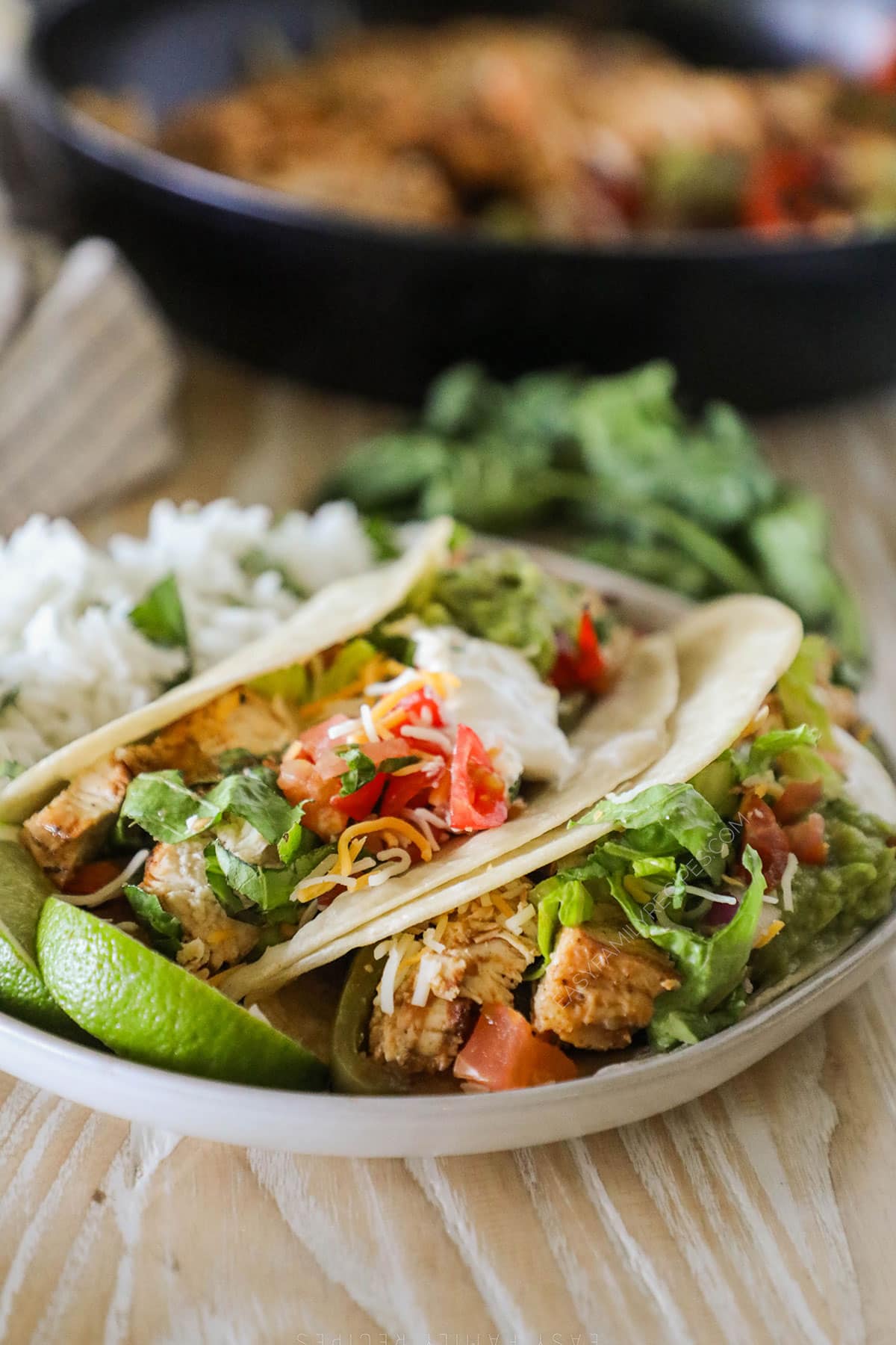 Chicken fajita tacos on a white plate with a lime wedge and cilantro in the background.