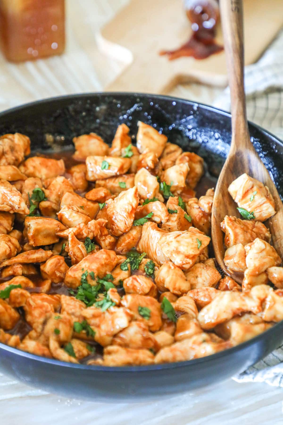 Honey BBQ Chicken Bites in a black skillet with a wooden spoon stirring them. 