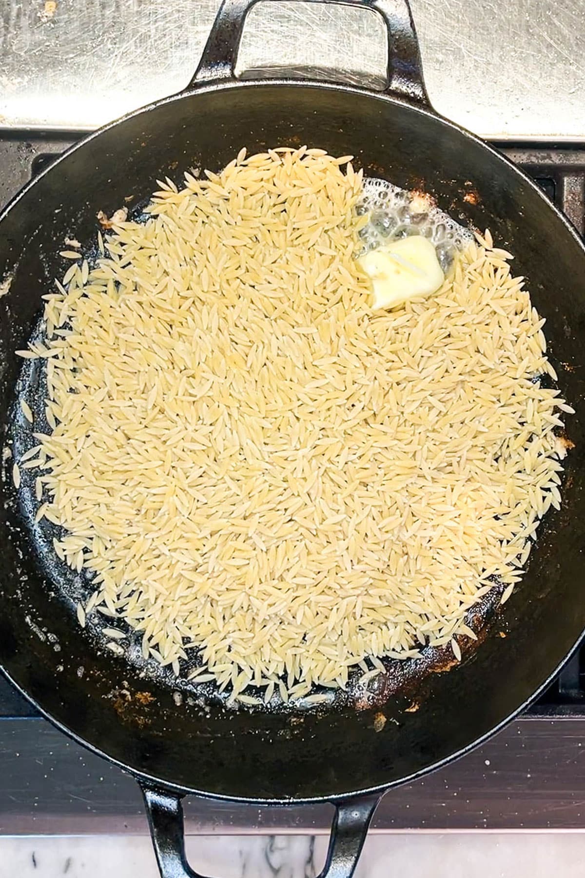 Step 2 for making lemon chicken orzo - add the orzo and butter to the skillet.