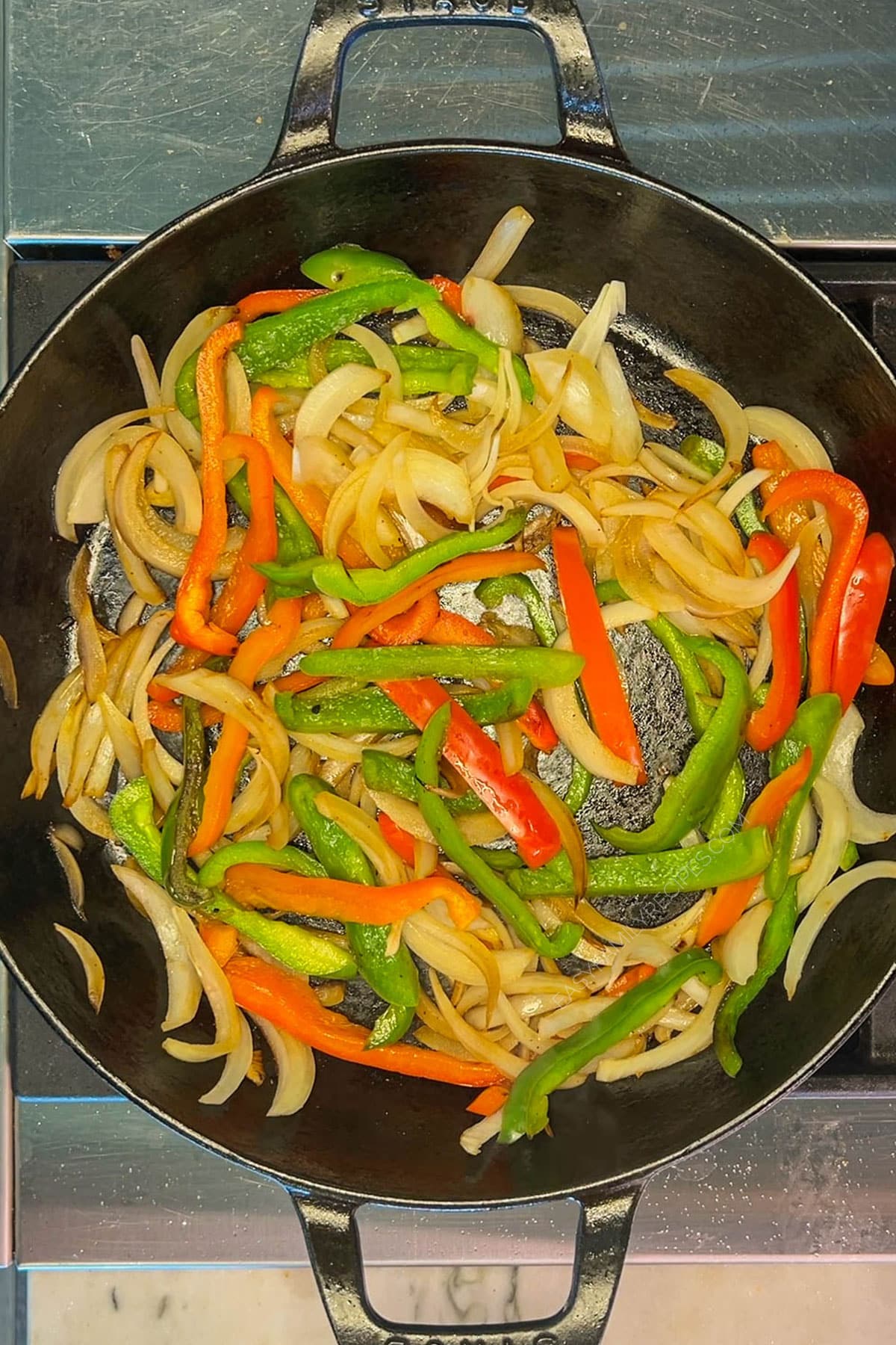 Onion and peppers sauteed in a skillet for fajita tacos.