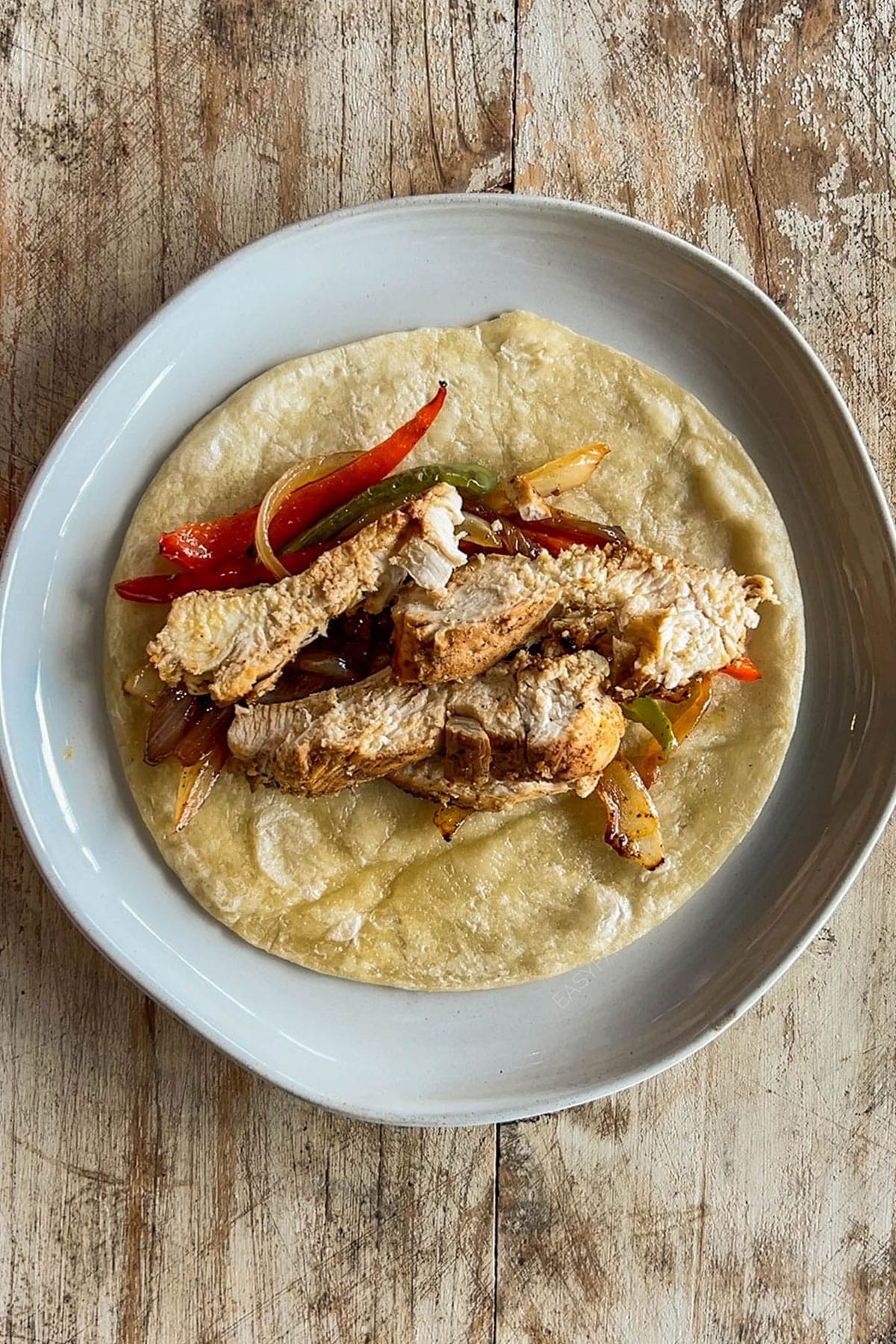 Top view of a plate with a tortilla and chicken strips for chicken fajita tacos