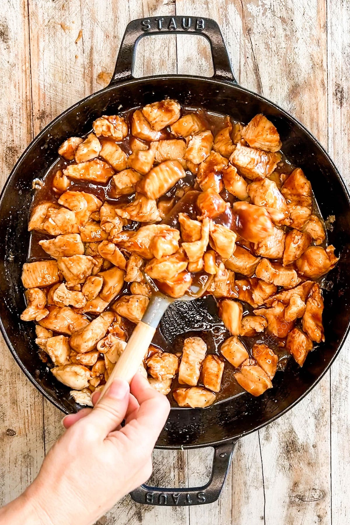 Stirring the chicken bites in a black skillet for honey BBQ chicken bites.