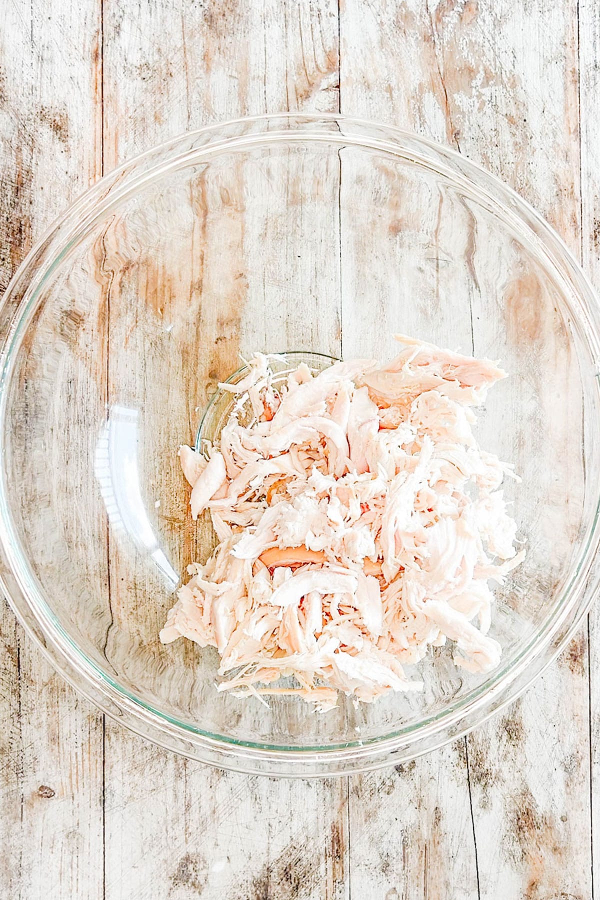 Top view of shredded chicken in a glass mixing bowl for Street Corn Chicken Salad