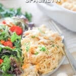 A white plate with a serving of baked chicken spaghetti and a side salad on a whitewashed background. The text reads, “Baked Chicken Spaghetti”