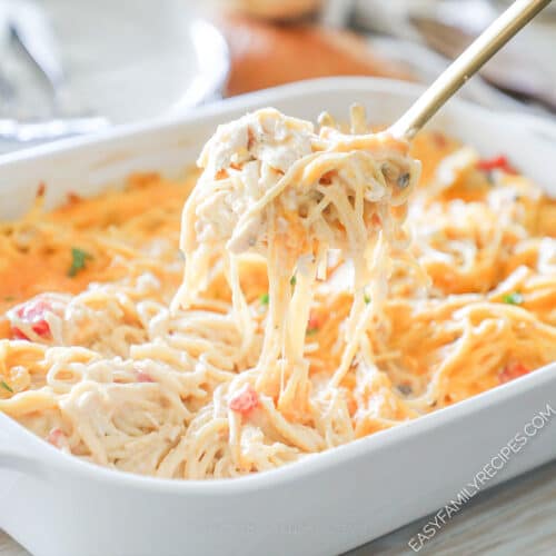 A serving spoon scoops a portion of baked chicken spaghetti out of the casserole dish.