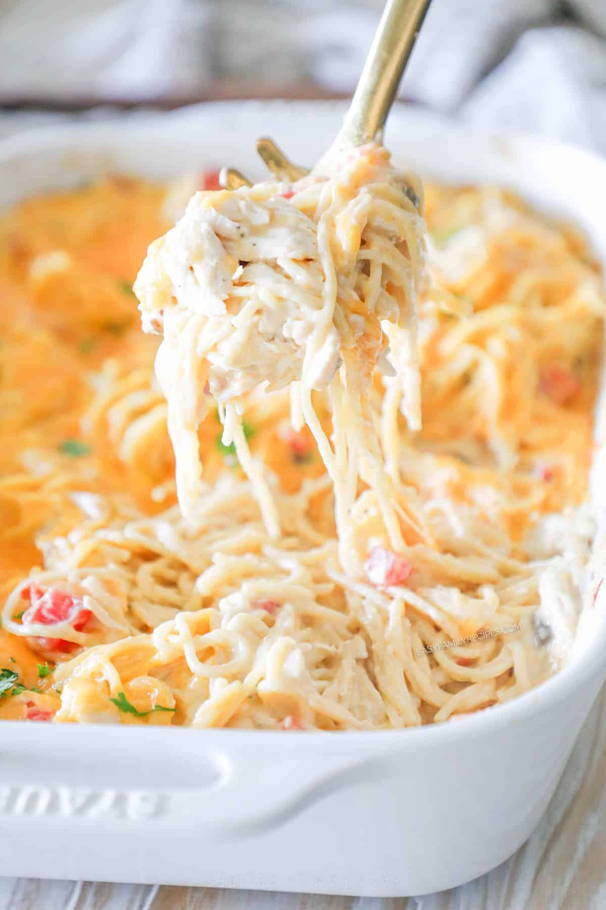 A serving spoon scoops a portion of baked chicken spaghetti out of the casserole dish.