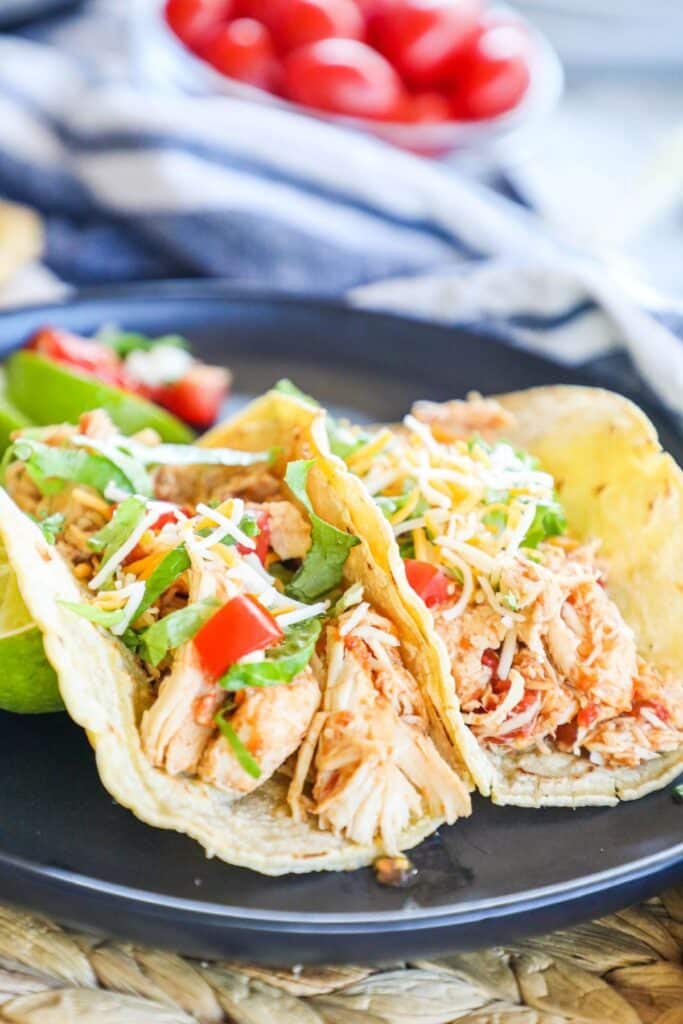 2 shredded chicken tacos on a black plate